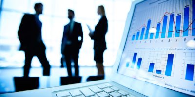 Financial document in laptop on background of three business partners interacting