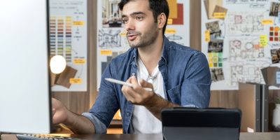 smart adult caucasian designer with beard sitting on working table desk video conference with clients, young smart creative designer working at home ,home isolation quarantine concept